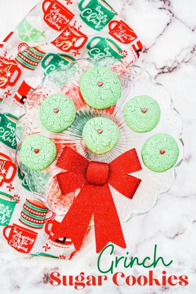 A glass tray of Grinch cookies with the words "Grinch Sugar Cookies" in green and red lettering.