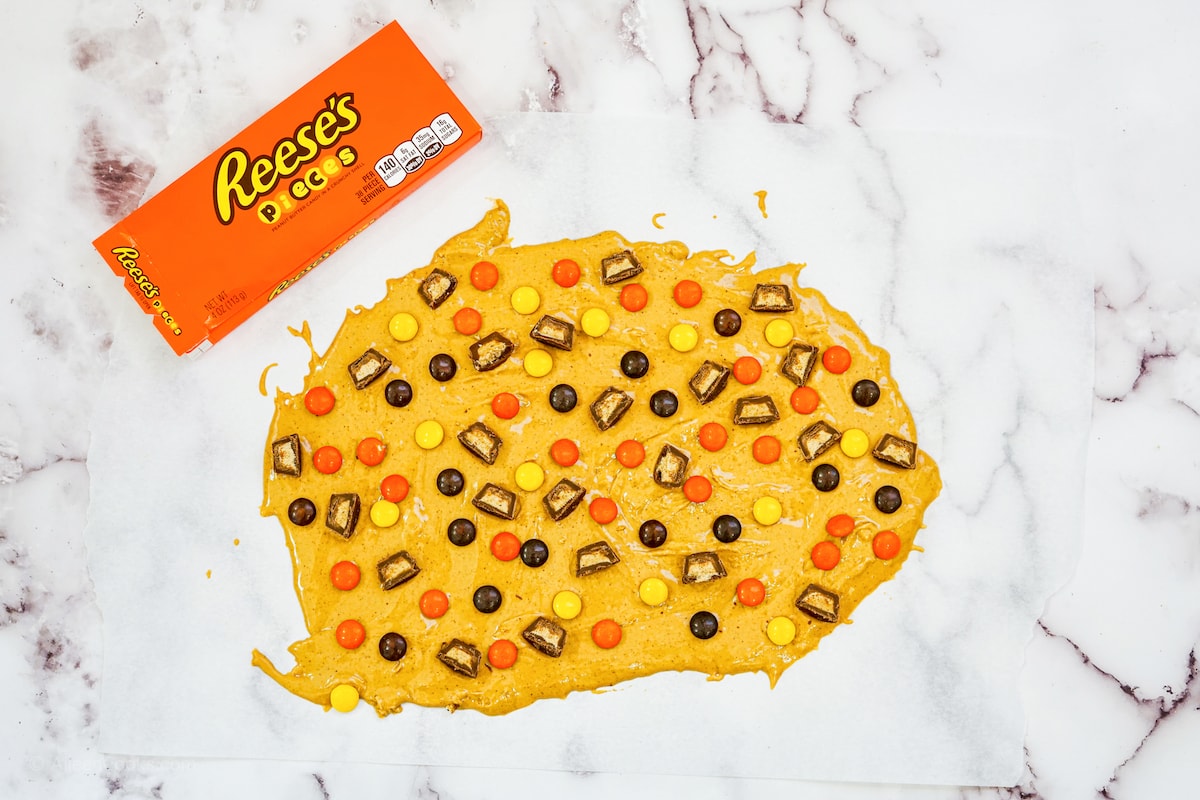 Peanut butter bark batter topped with mini peanut butter cups and Reeses pieces.