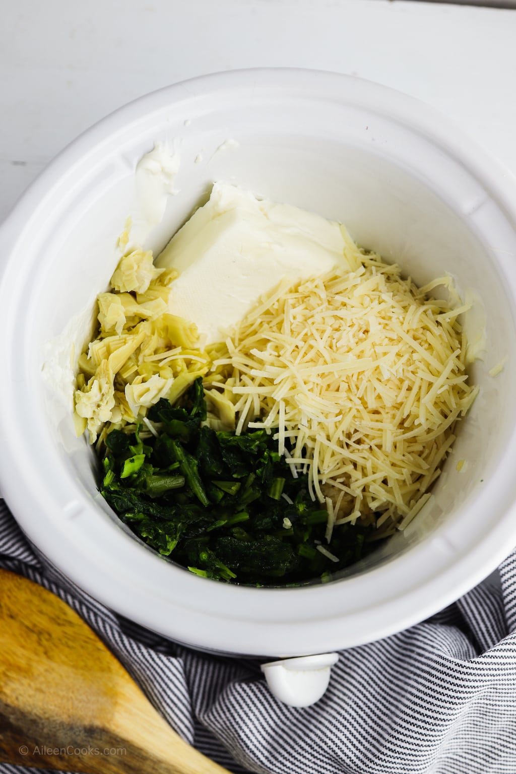 Cream cheese, parmesan cheese, spinach, and artichoke hearts inside of a slow cooker.