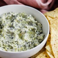 A bowl of spinach dip next to yellow tortilla chips.