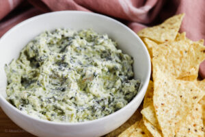 A bowl of spinach dip next to yellow tortilla chips.