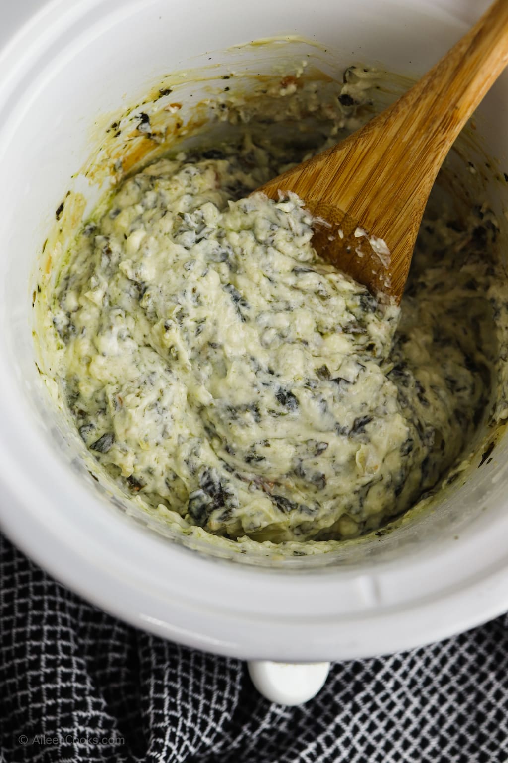 A wooden spoon mixing up the ingredients for spinach artichoke dip.