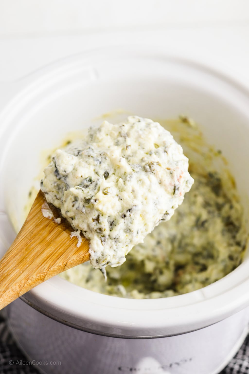 A spoonful of spinach artichoke dip held over a crock pot filled with the dip.