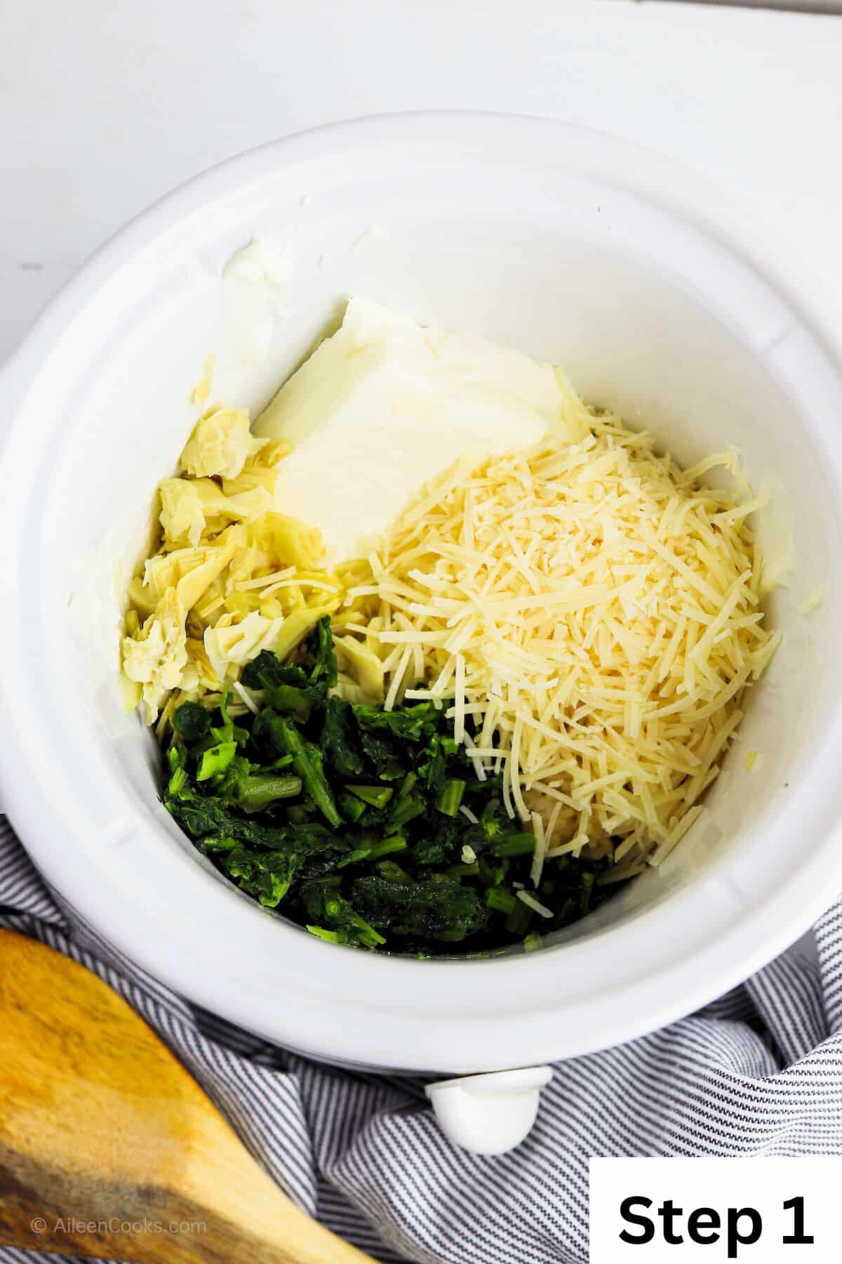 A white crockpot with spinach, parmesan cheese, artichoke hearts, and cream cheese inside.