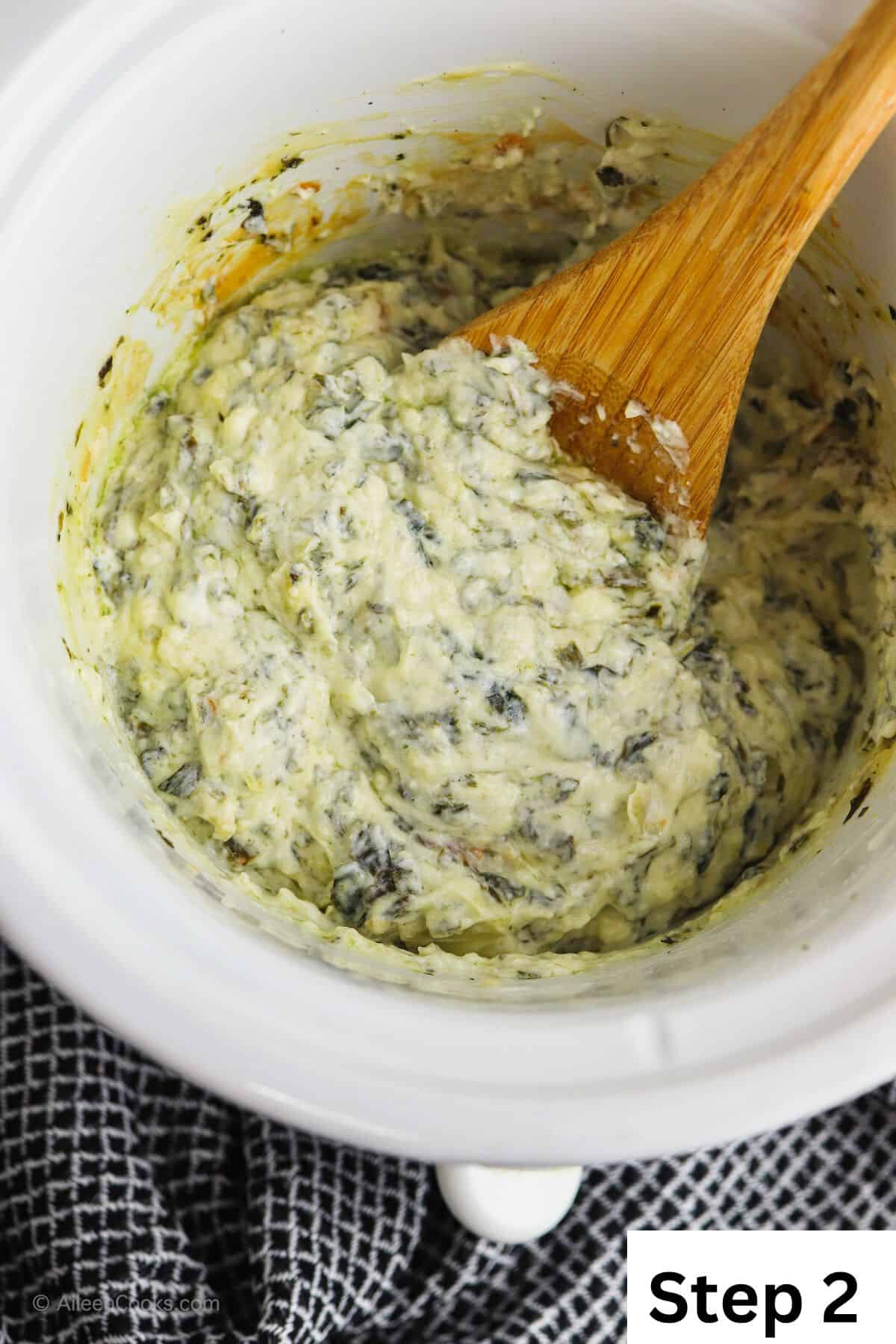 Ingredients for spinach artichoke dip mixed up inside a crock pot.