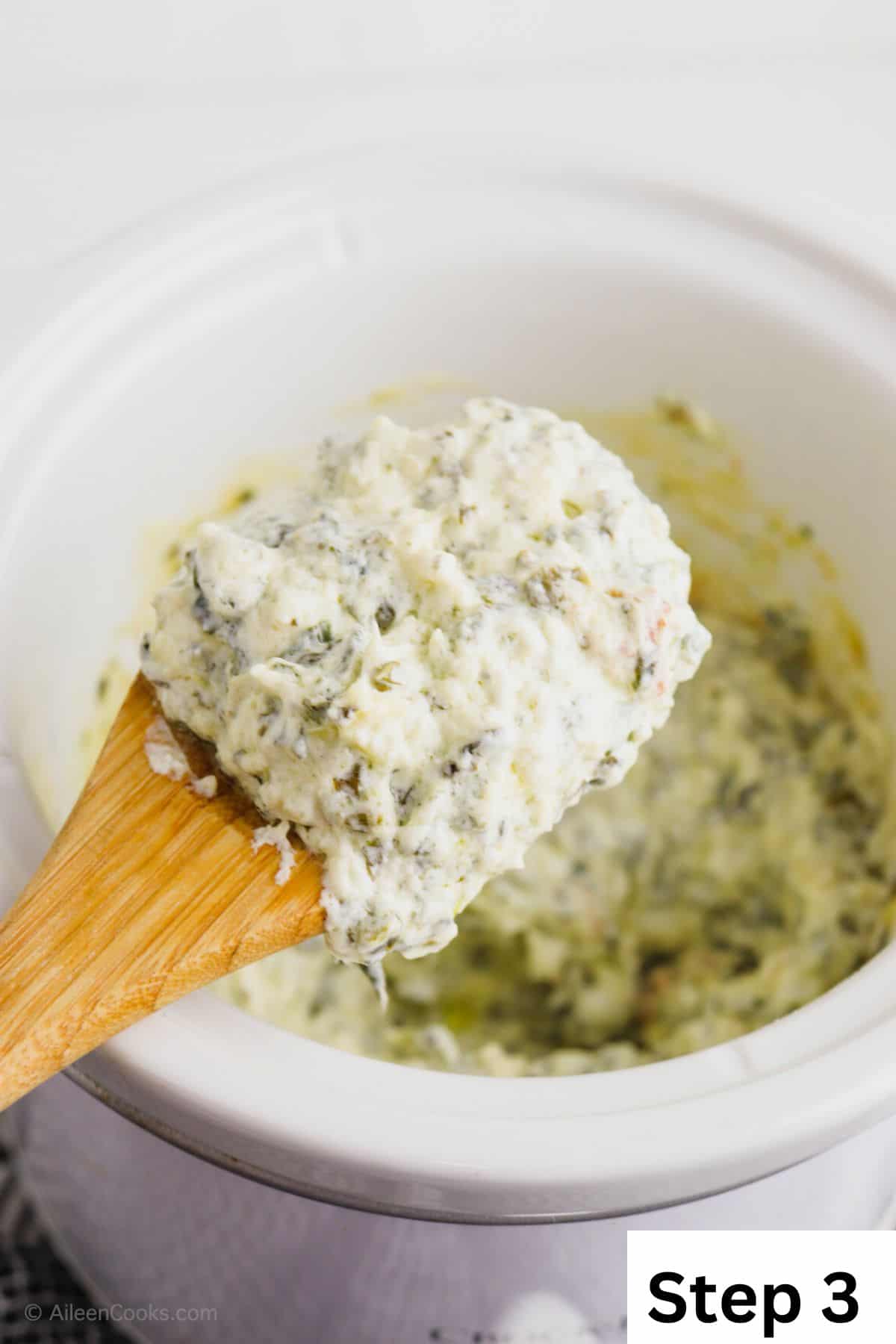 A wooden spoon holding up a spoonful of spinach artichoke dip.