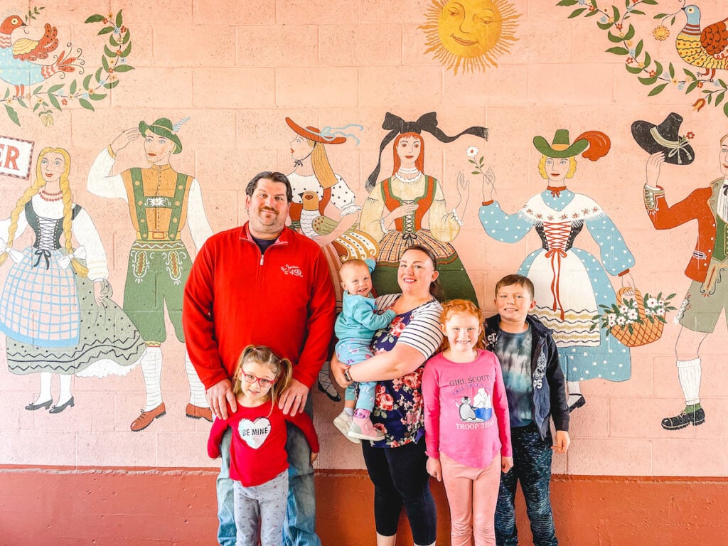 A family of 6 standing in. front of a mural. of dutch people.