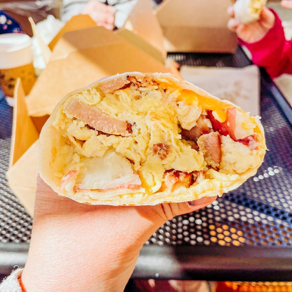 A hand holding up 1/2 of a breakfast burrito with sausage.