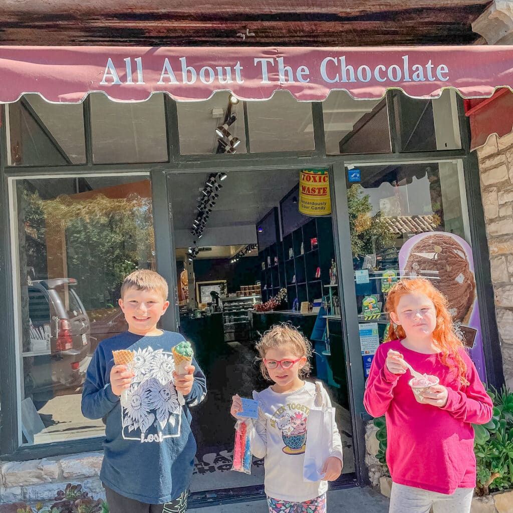 Three kids holding treats in front of All About The Chocolate in Carmel, CA.