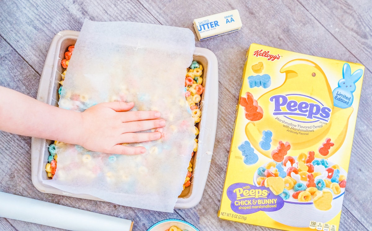 A hand pressing wax paper onto a baking dish of peeps cereal bars.
