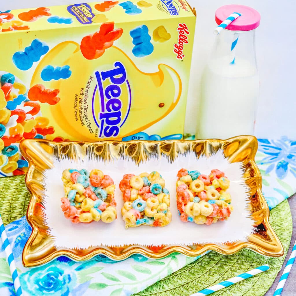 A dish of colorful cereal bars next to a glass bottle of milk.