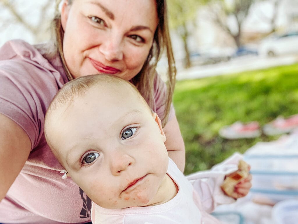 A mom and baby sitting on grass having a picnic.