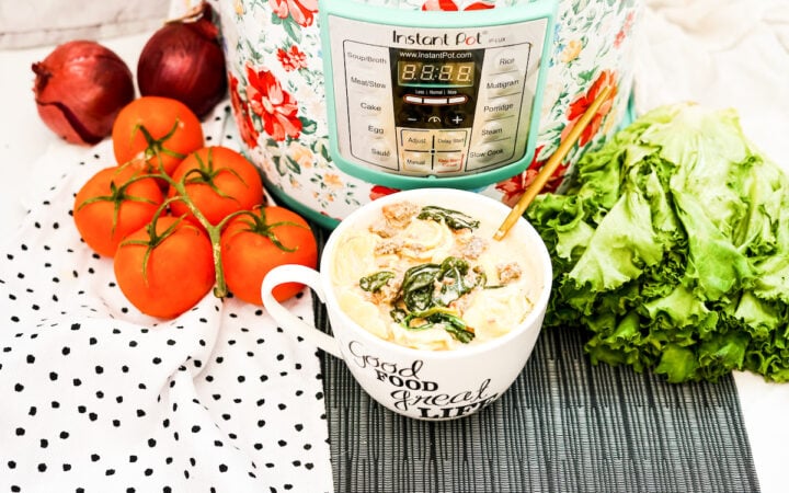 A bowl of tortellini soup in front of an instant pot and next to fresh tomatoes and lettuce leaves.