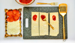 Pizza sauce spread over half of each of three puff pastry strips.