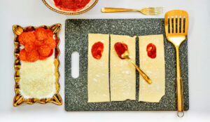 Pizza sauce spread over half of each of three puff pastry strips.