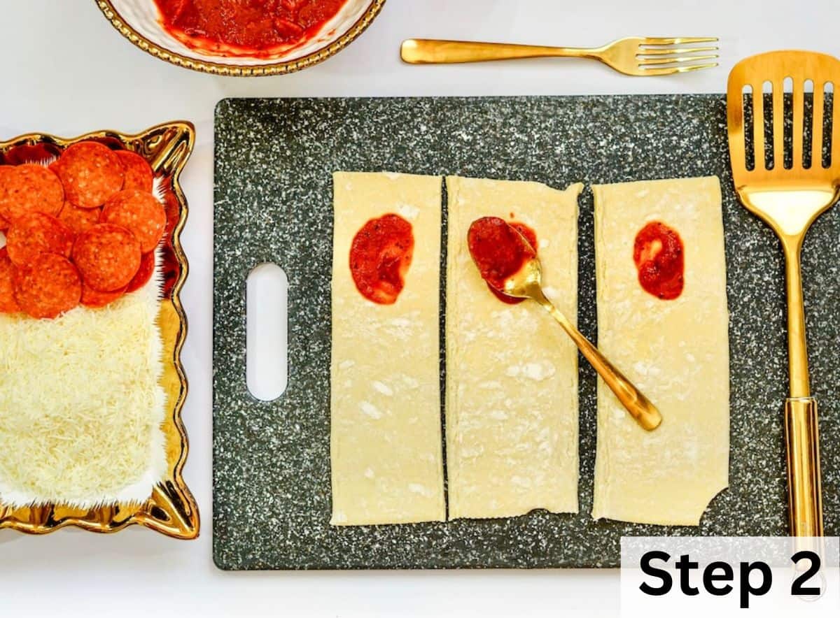 A small amount of pizza sauce spread on half of each of three puff pastry strips.