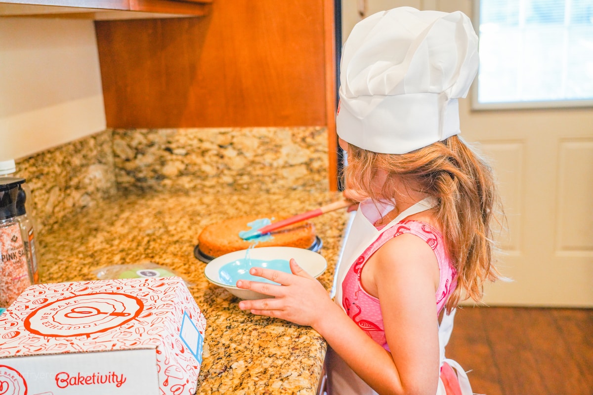 A girl spreading blue icing onto a cookie cake.