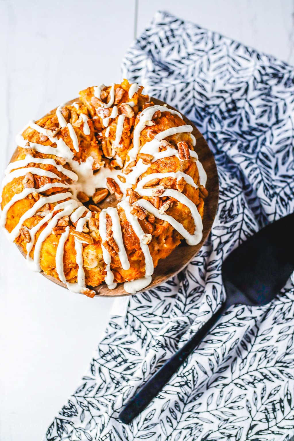 Overhead picture of golden brown monkey bread drizzled with a white frosting next to a blue and white tea towel.