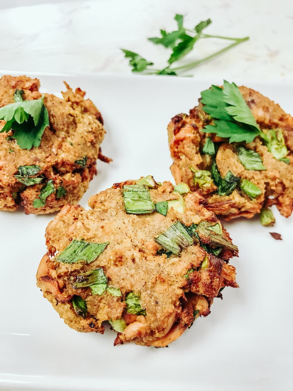 Three salmon cakes on a white plate, garnished with parsley