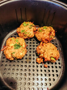 Four salmon cakes laid out in a single layer in the basket of an air fryer, baked and ready to be served.