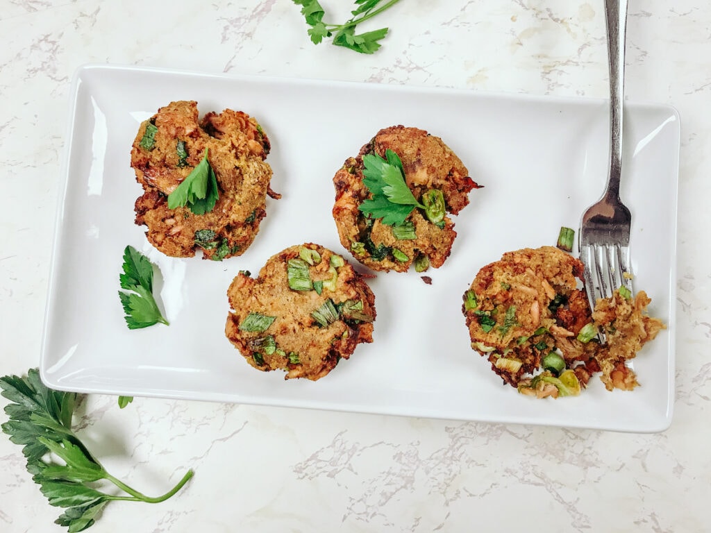 A plate of air fryer salmon cakes, garnished with parsley and on a marble background