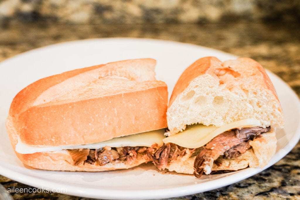 A closeup photo of a French Dip sandwich on a white plate, cut in half