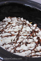 Mini marshmallows with hot fudge chocolate drizzled on top, sitting in the inside of a slow cooker