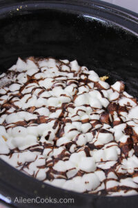 Mini marshmallows with hot fudge chocolate drizzled on top, sitting in the inside of a slow cooker