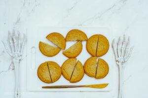 Sugar cookies cut in half on a white cutting board, with a gold knife, sitting on a marble countertop.