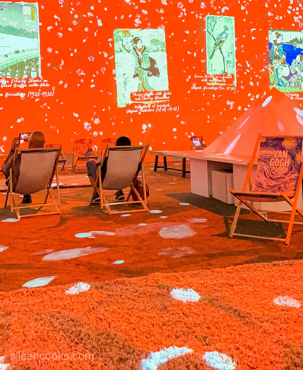A room with several area rugs and pictures of van Gogh's are projected on the wall in red colors.