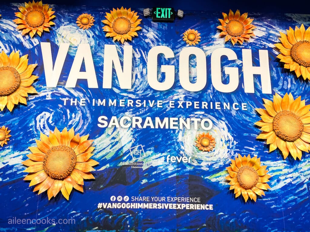 A mural with large sunflowers and the words "Van Gogh The Immersive Experience" in white letters.