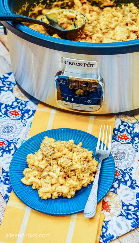 Cheeseburger mac and cheese served on a blue plate, sitting on a yellow table runner and with a crockpot in the background