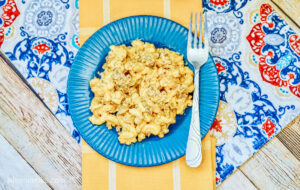 Bird’s eye view of a serving of cheeseburger mac and cheese served on a blue plate with a fork, sitting on a beautiful table laid out with a yellow table runner and blue patterned place mat.