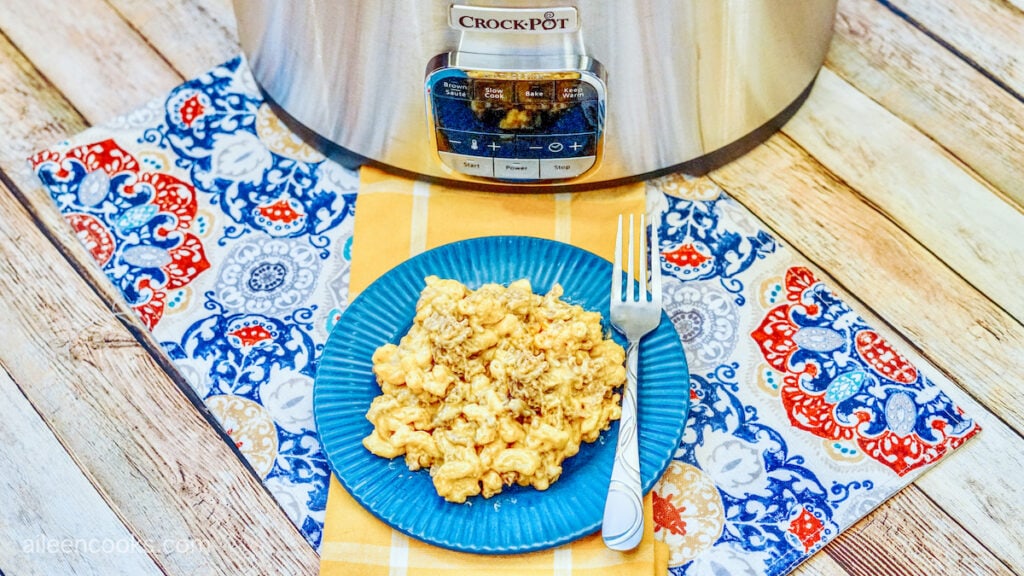 Cheeseburger mac and cheese served on a blue plate, sitting on a yellow table runner and with a crockpot in the background