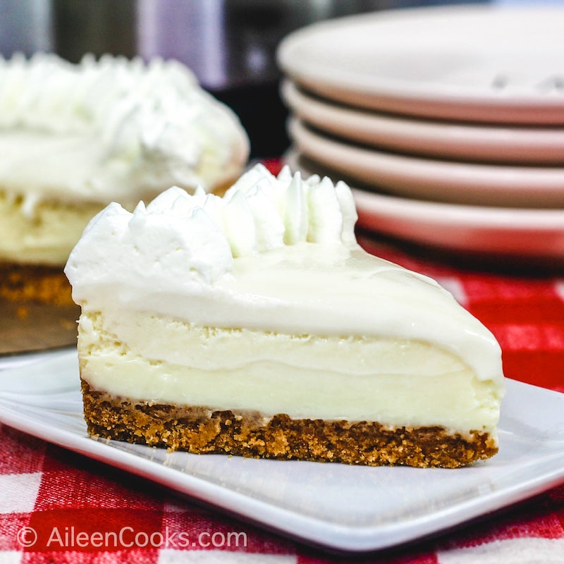 A slice of Instant Pot Cheesecake sitting on a square white plate, sitting on a plaid red tablecloth