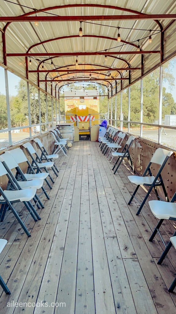 An open air train car with white chairs and open windows. 