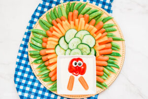 A Turkey Veggie Tray, with a range of different veggies, sitting on a large round platter, laying on a blue plaid tea towel.