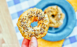 A hand holding up half of an air fryer bagel, with the other half in the background on a blue plate