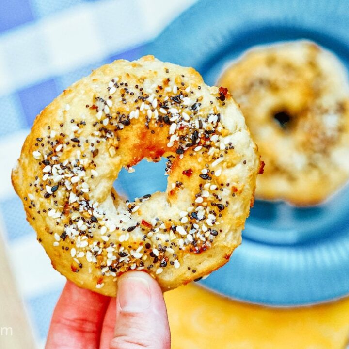 A hand holding up half of an air fryer bagel, with the other half in the background on a blue plate