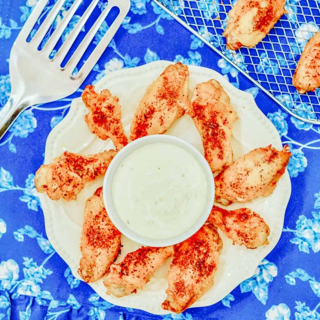 A white scalloped edged plate filled with dry rubbed chicken wings and a bowl of white dip.
