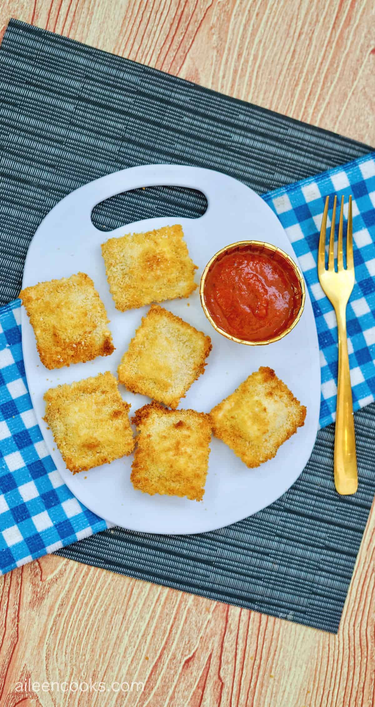 A white platter filled with golden brown air fried ravioli next to a small bowl of marinara sauce.