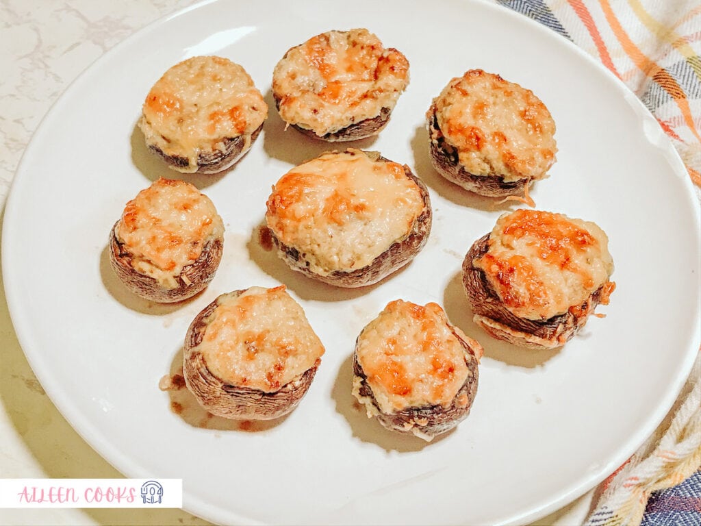 A batch of air fryer stuffed mushrooms placed on a white plate with a colorful plaid tea towel placed underneath