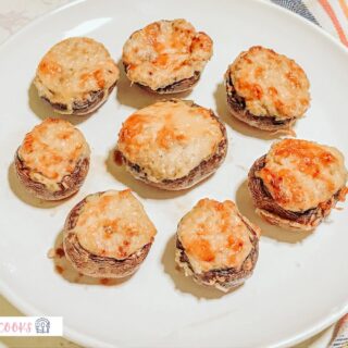 A batch of air fryer stuffed mushrooms placed on a white plate with a colorful plaid tea towel placed underneath