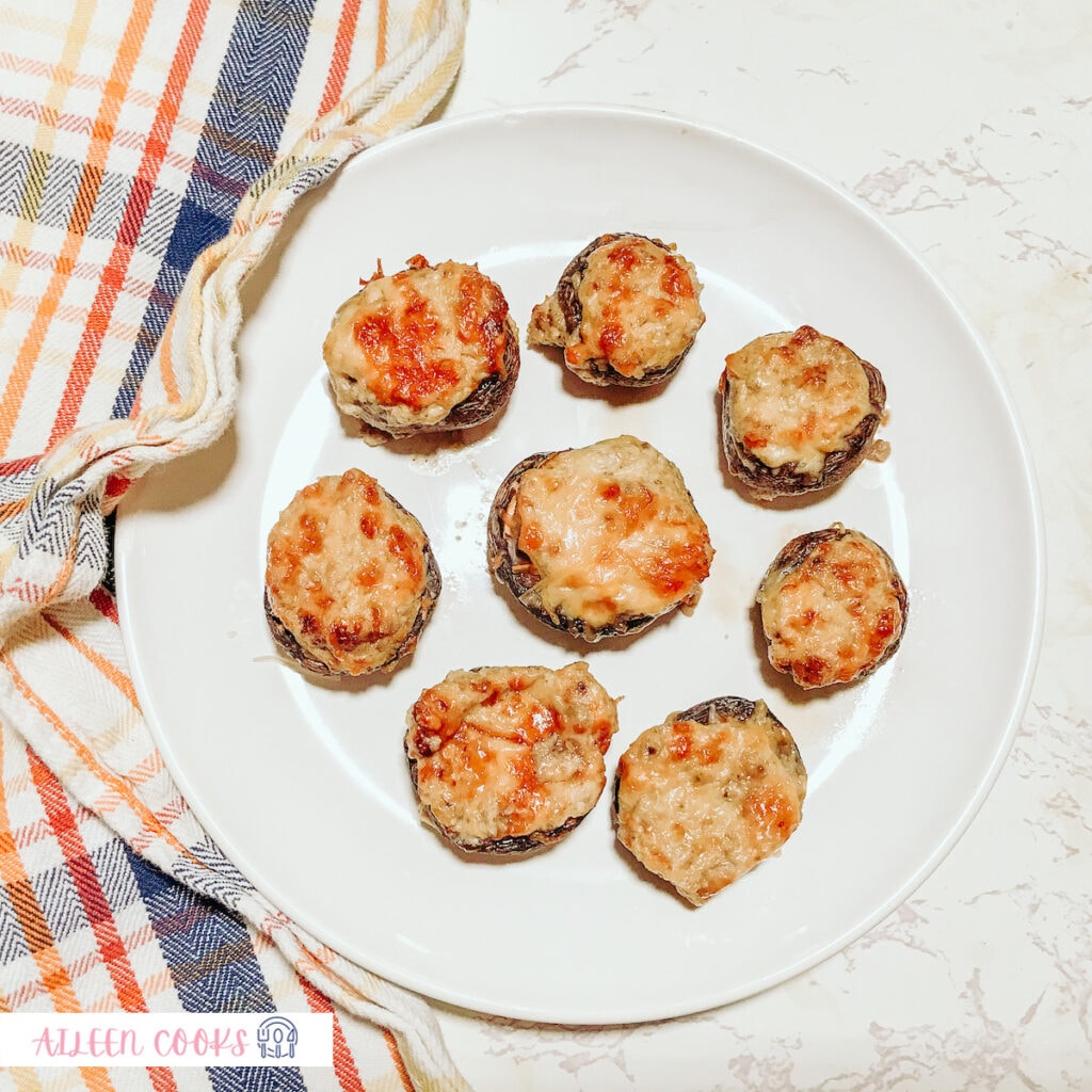 Bird’s eye view of stuffed mushrooms, cooked from the air fryer, served on a white plate sitting on a marble countertop