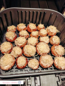 A batch of stuffed mushrooms placed in a single layer in the inner basket of an air fryer, ready to be baked