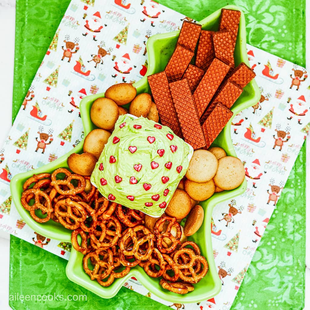 A bird’s eye view of cookie dip, topped with heart-shaped sprinkles, and served in a Christmas tree-shaped platter with cookies, pretzels and wafers