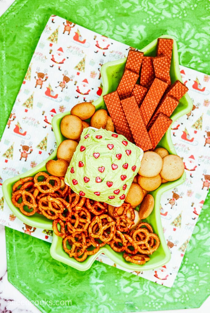 Aerial view of green cookie dip, garnished with heart-shaped sprinkles and surrounded by cookies, pretzels and wafer cookies.