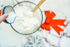 Adding milk to a glass bowl full of ingredients to make cookie dip