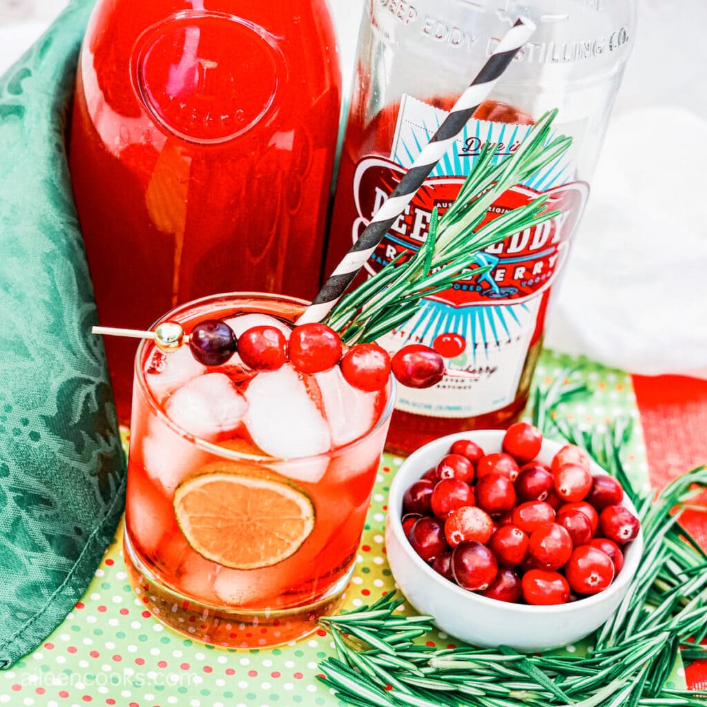 Bird’s eye view of a Christmas Moscow Mule in a cocktail glass, surrounded by a bottle of cranberry vodka and a bowl of fresh cranberries