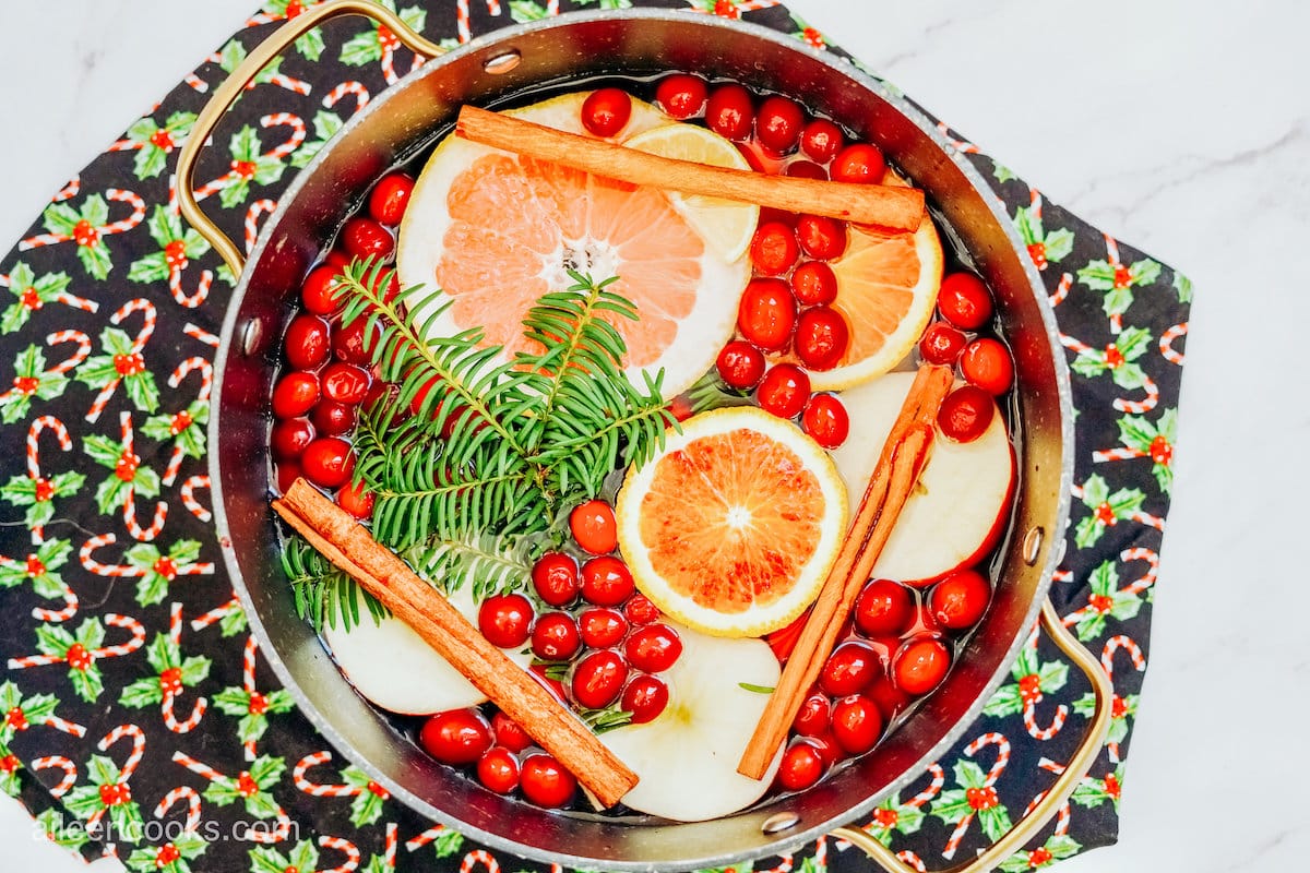 Aerial view of a simmer pot, filled with ingredients to give a holiday-themed aroma, sitting atop a holiday-themed placemat